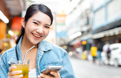 Portrait of smiling young woman drinking drink in city
