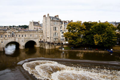 Arch bridge over river amidst buildings against sky