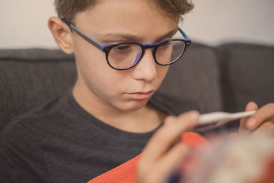 Close-up of boy looking at thermometer while sitting on sofa at home