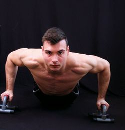 Portrait of shirtless young man exercising against black background