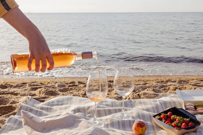 Woman's hand pouring rose wine in a glass. romantic picnic on the beach near the sea.