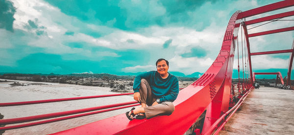 Full length of young man sitting against sky