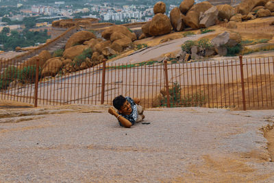 Rear view of man sitting on rock by road