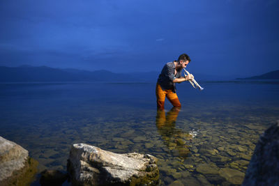 Side view of man standing on rock against sky