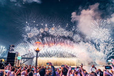 Crowd photographing sydney harbor bridge and fireworks in city at night