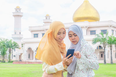 Women using mobile phone against building