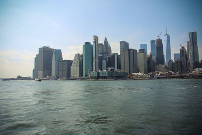 Sea by modern buildings in city against sky
