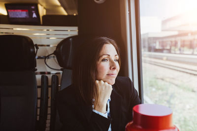 Portrait of mid adult woman looking away while sitting on window