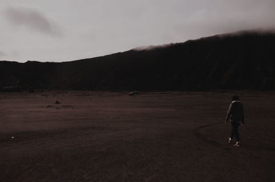 Rear view of man walking on field against sky