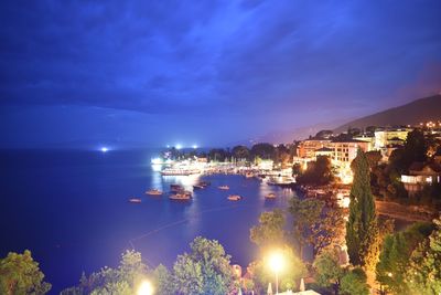 Illuminated city by sea against sky at night