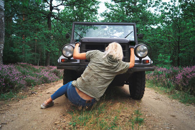 Woman sitting on road by breakdown jeep in forest