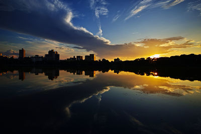 Silhouette buildings by lake against sky during sunset