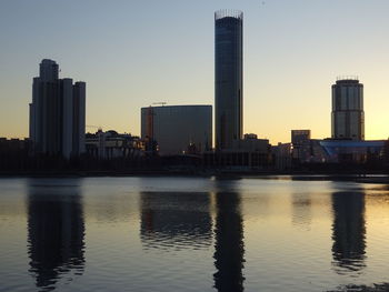 Buildings by river against sky during sunset