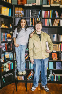Smiling girl standing next to male friend holding book near shelf in bookstore