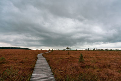 Dirt road on field against sky