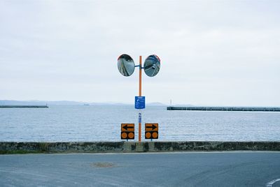 Road sign by sea against sky