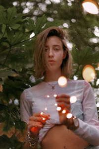 Portrait of young woman looking at illuminated tree