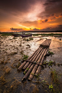 Wooden raft floating in lake against sky during sunset