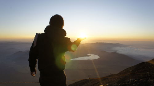 Optical illusion of silhouette man holding sun against sky during sunset