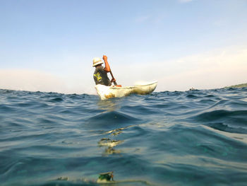 Rear view of man in canoe on sea against sky