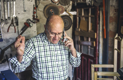 Carpenter talking on phone while standing in workshop