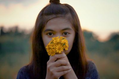 Close-up portrait of young woman holding yellow flowers during sunset