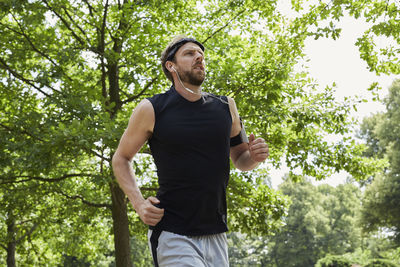 Man listening music while running against trees in park