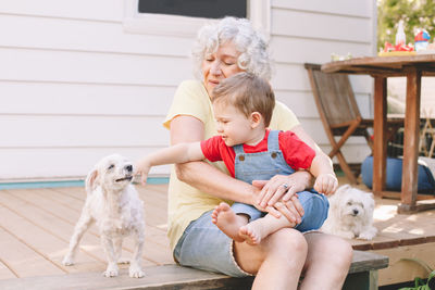 Happy senior woman sitting with grandson and dog outdoors