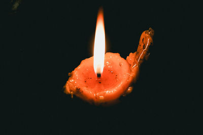Close-up of orange burning candle against black background