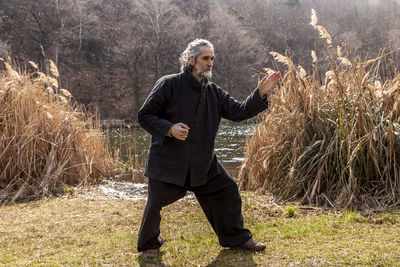 Mature man practicing tai chi discipline outdoors in a lake park on a winter day