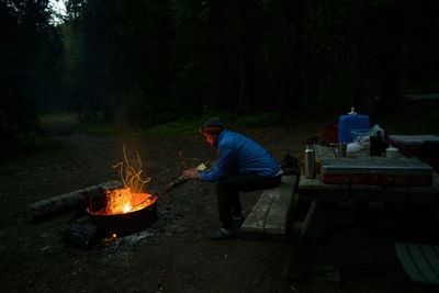 Side view of hiker warming hands by campfire at campsite during dusk