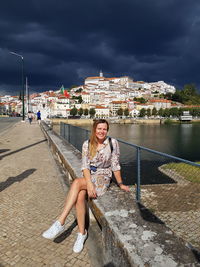 Full length portrait of woman sitting in city against sky