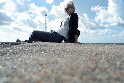 Low angle view of young woman sitting on shore against sky