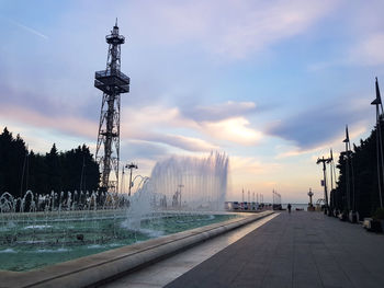 Fountain by city against sky during sunset