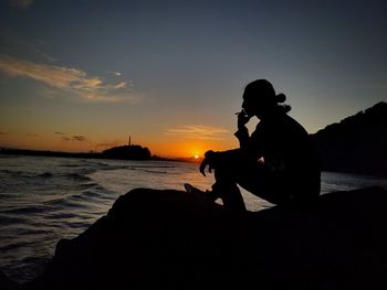 Silhouette people sitting on beach against sky during sunset