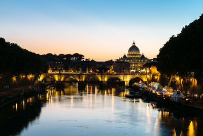 Illuminated bridge over river by buildings against sky in city