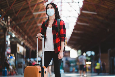 Low angel view of young woman wearing mask standing at airport