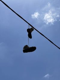 Low angle view of shoes hanging on cable against sky