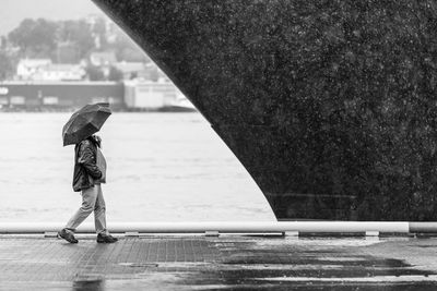 Man walking with umbrella on wet sidewalk by cruise ship during monsoon