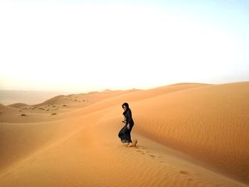 Man on sand dune in desert against clear sky