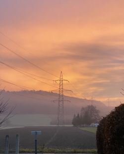 Electricity pylons against sky during sunset