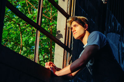 Portrait of young man looking away while sitting on railing