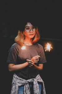 Young woman using mobile phone while standing against black background