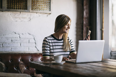 Young woman using phone while sitting on table