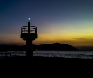 Silhouette of lighthouse by sea against sky at dusk