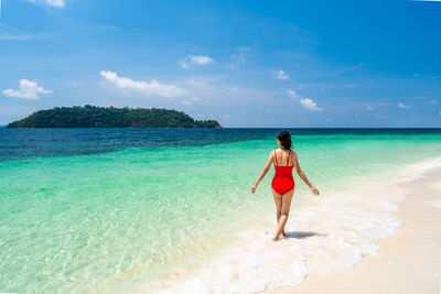 Rear view of woman standing at beach against sky