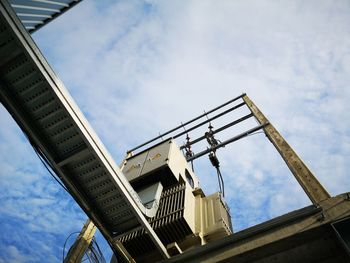 Low angle view of crane by building against sky