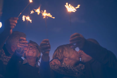 Low angle view of senior couple playing with sparklers against sky at night