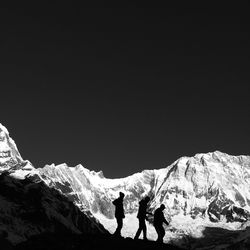 People walking by snowcapped mountains against clear sky