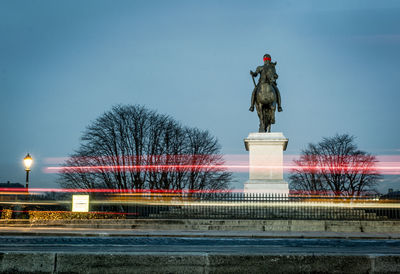 Light trails over street at pont neuf against statue and clear sky at dusk